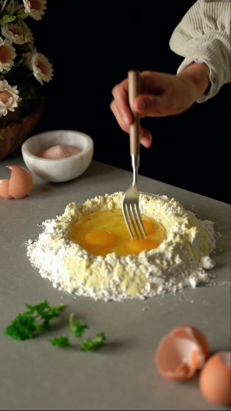A chef hand mixes eggs and flour on a countertop, preparing fresh pasta dough.