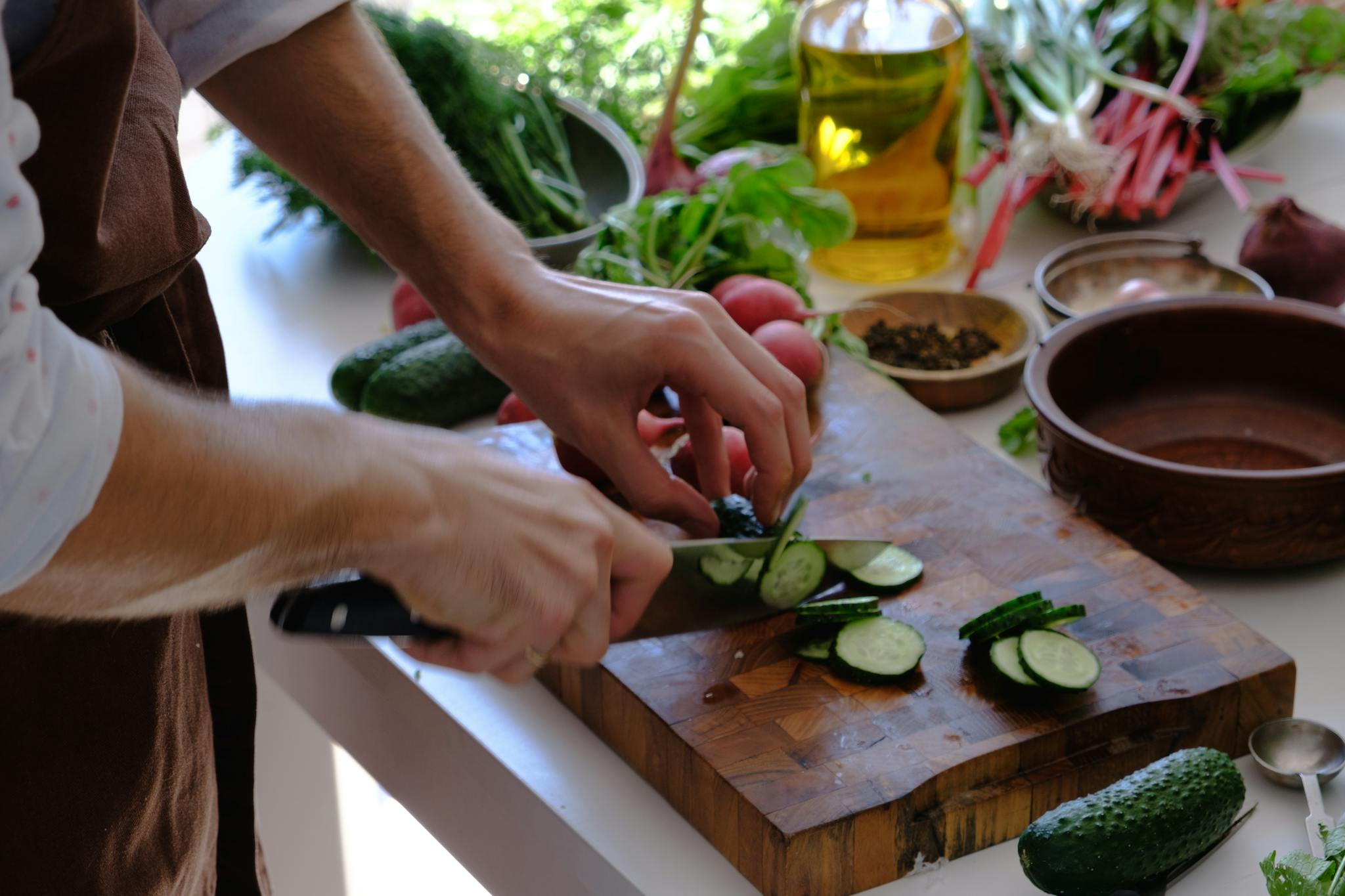 A close-up of hands slicing a cucumber on a wooden chopping board in a kitchen setting.