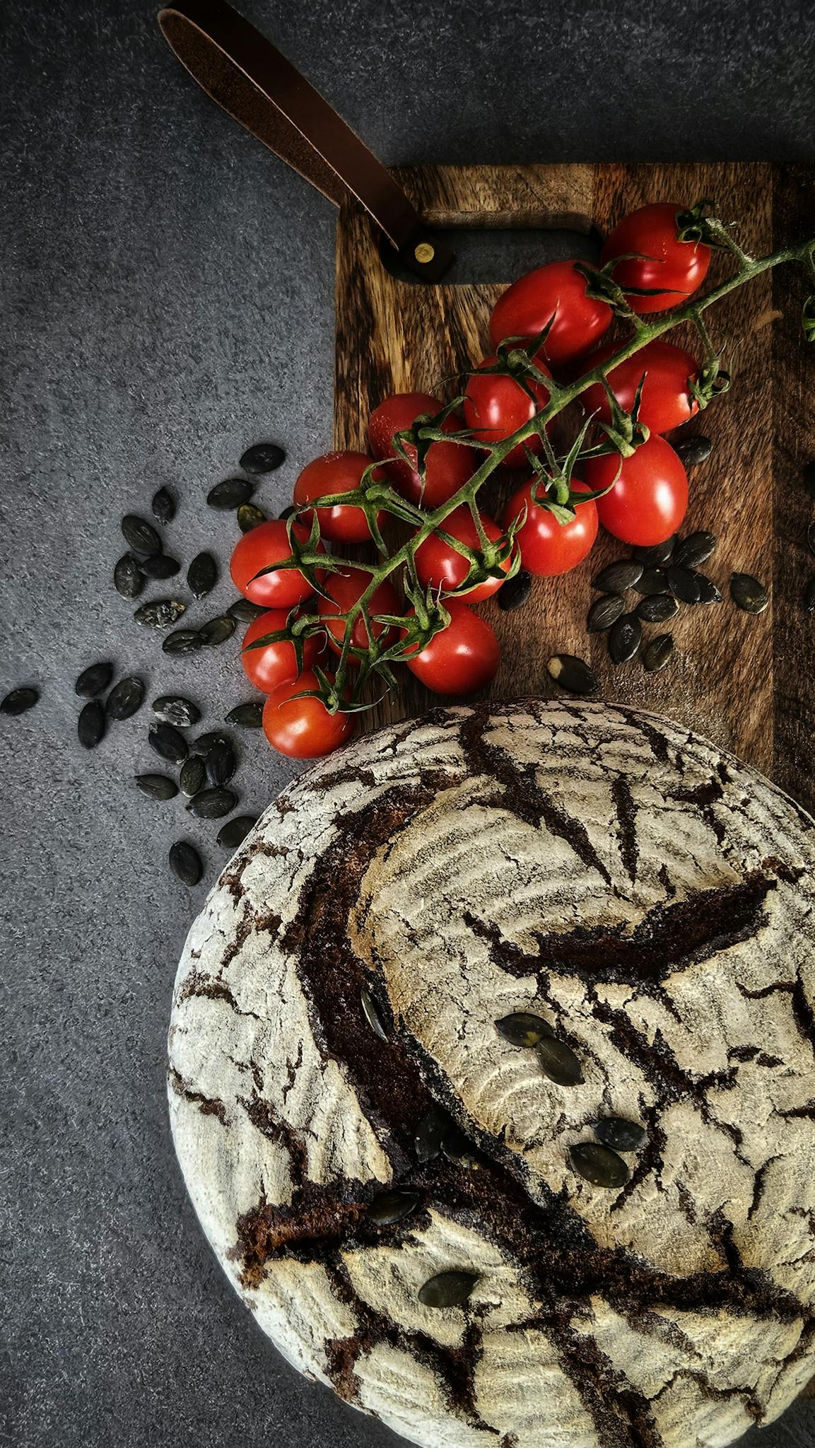 Artisan bread with pumpkin seeds on a wooden board, paired with fresh cherry tomatoes.