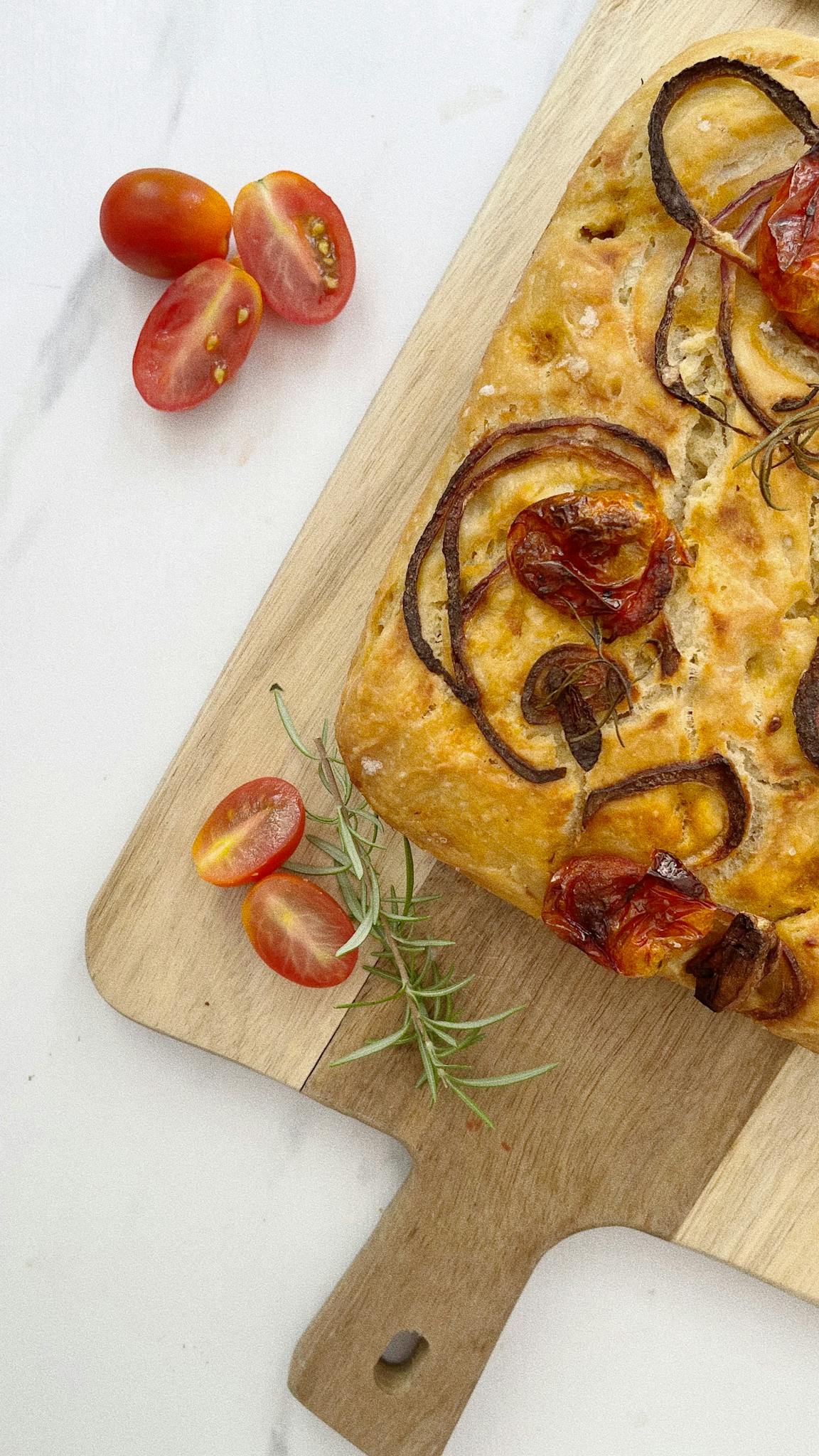 Delicious homemade focaccia topped with roasted tomatoes and onions on a wooden board.